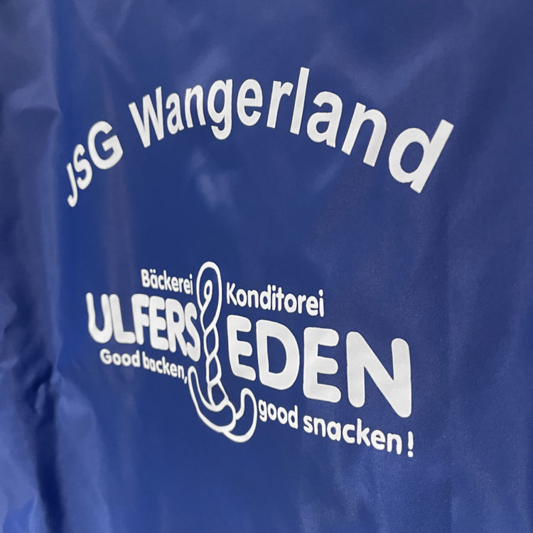 weißer Vereinsname und Sponsorenwerbung auf einer blauen Regenjacke