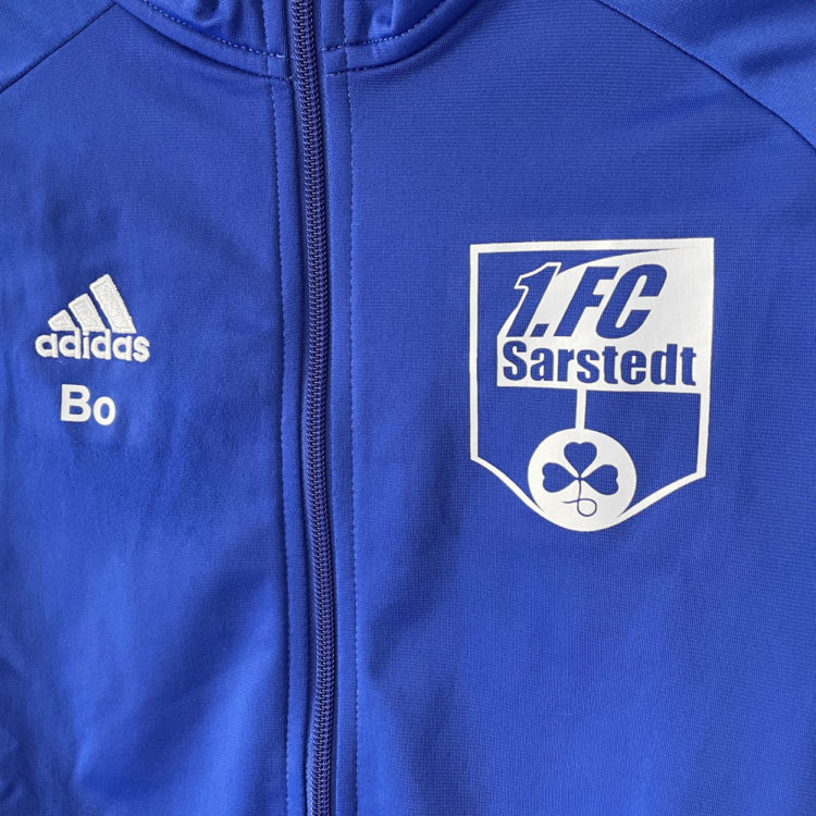 Die adidas Trainingsjacken für Kinder haben den Vereinslogo Aufdruck und die Initialen der Kids