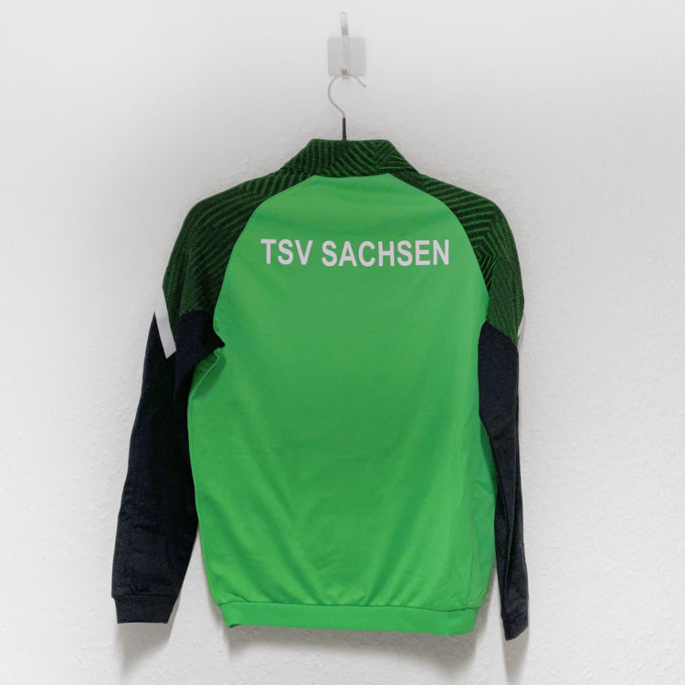 grüne Jako Trainingsjacke mit weißem Vereinsnamen des TSV Sachsen auf dem Rücken