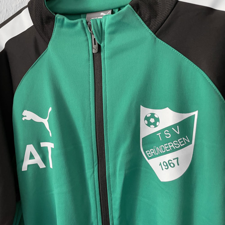 Die grüne Puma Trainingsjacke mit Vereinslogo und Initialen in weiß
