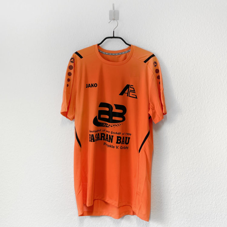 orangenes Fussball Trikot mit Vereinslogo und Werbung in schwarz